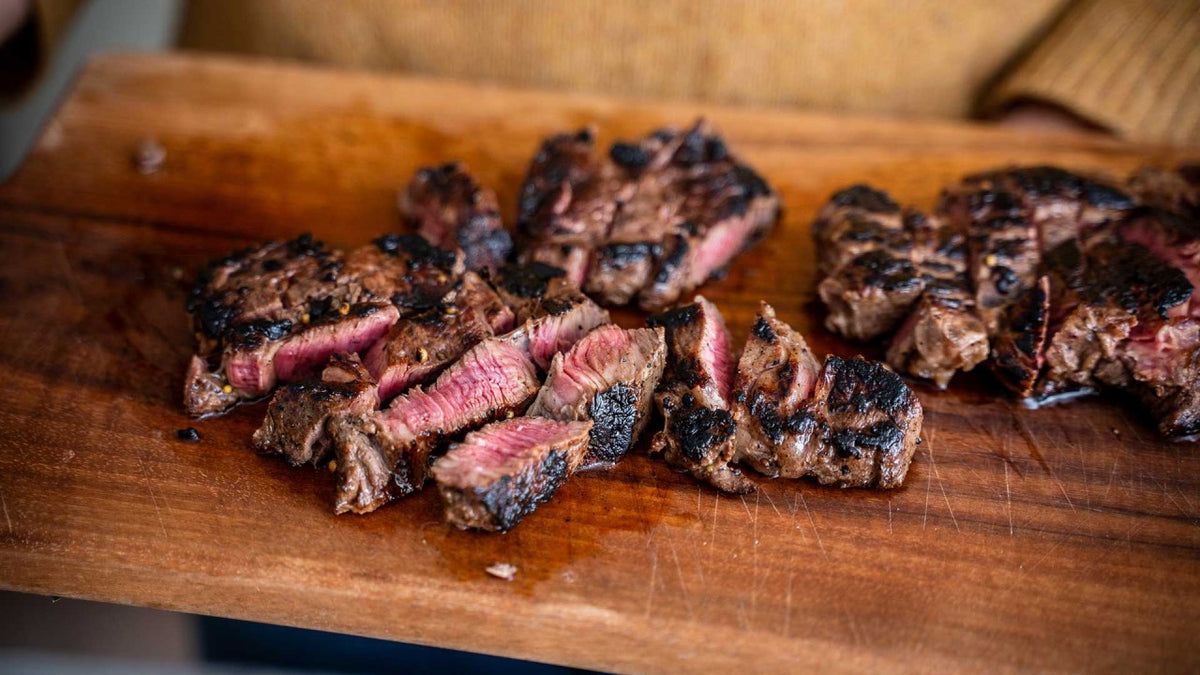 Ein gegrilltes Ribeye-Steak mit knuspriger Kruste und rosa Mitte auf einem Holzbrett.