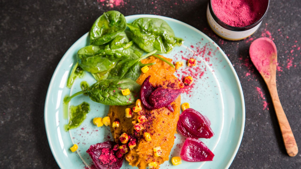 Teller mit Blattsalat, Polenta, geröstetem Mais, eingelegter Rote Bete und goldgelbem Rote-Bete-Pulver.
