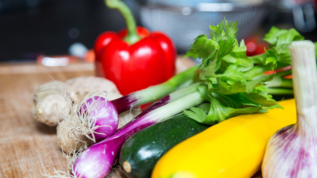 Rote Paprika, Zucchini und Knoblauch liegen auf einem Holzbrett.