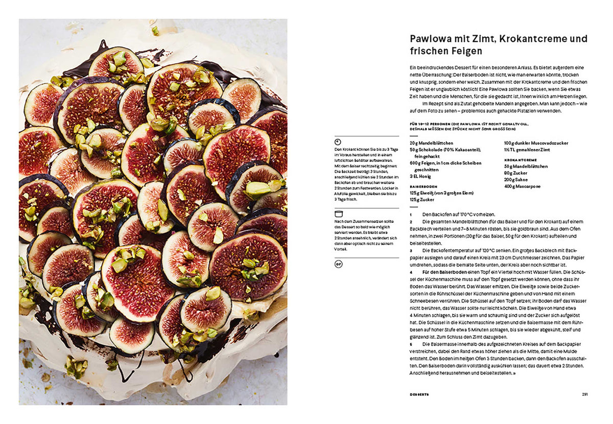 Eine Pavlova mit Feigen und Pistazien neben einer aufgeschlagenen Seite eines Rezeptbuchs.