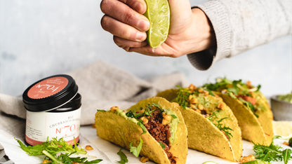 Hand presst Limette über Tacos mit Chili con Carne, daneben eine Dose Bio Churrasco Barbecue N°704.