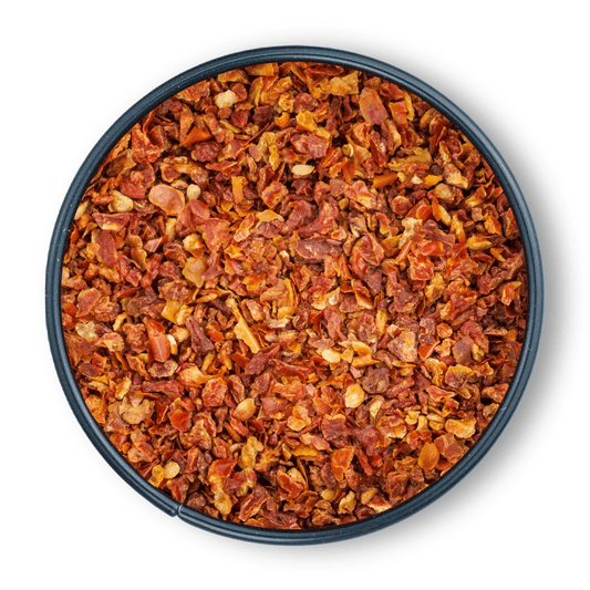 Schale mit groben Bio Tomatenflocken und Chili-Flocken auf weißem Hintergrund, Draufsicht.