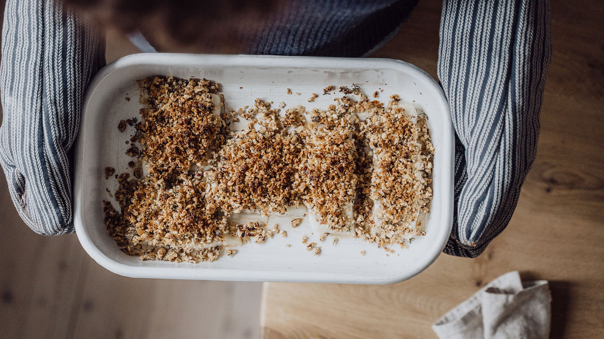 Die Auflaufform mit goldbraunem Streusel wird mit Ofenhandschuhen gehalten; einige Teile fehlen.